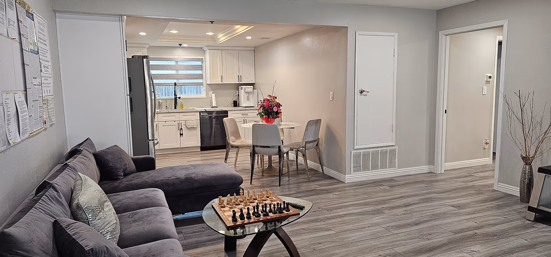 Cozy living area with a sofa, chessboard, and open kitchen in a senior facility.