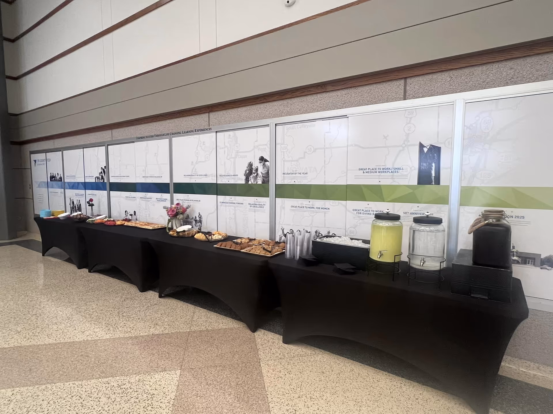 A long refreshment table with pastries and drinks in a hallway.