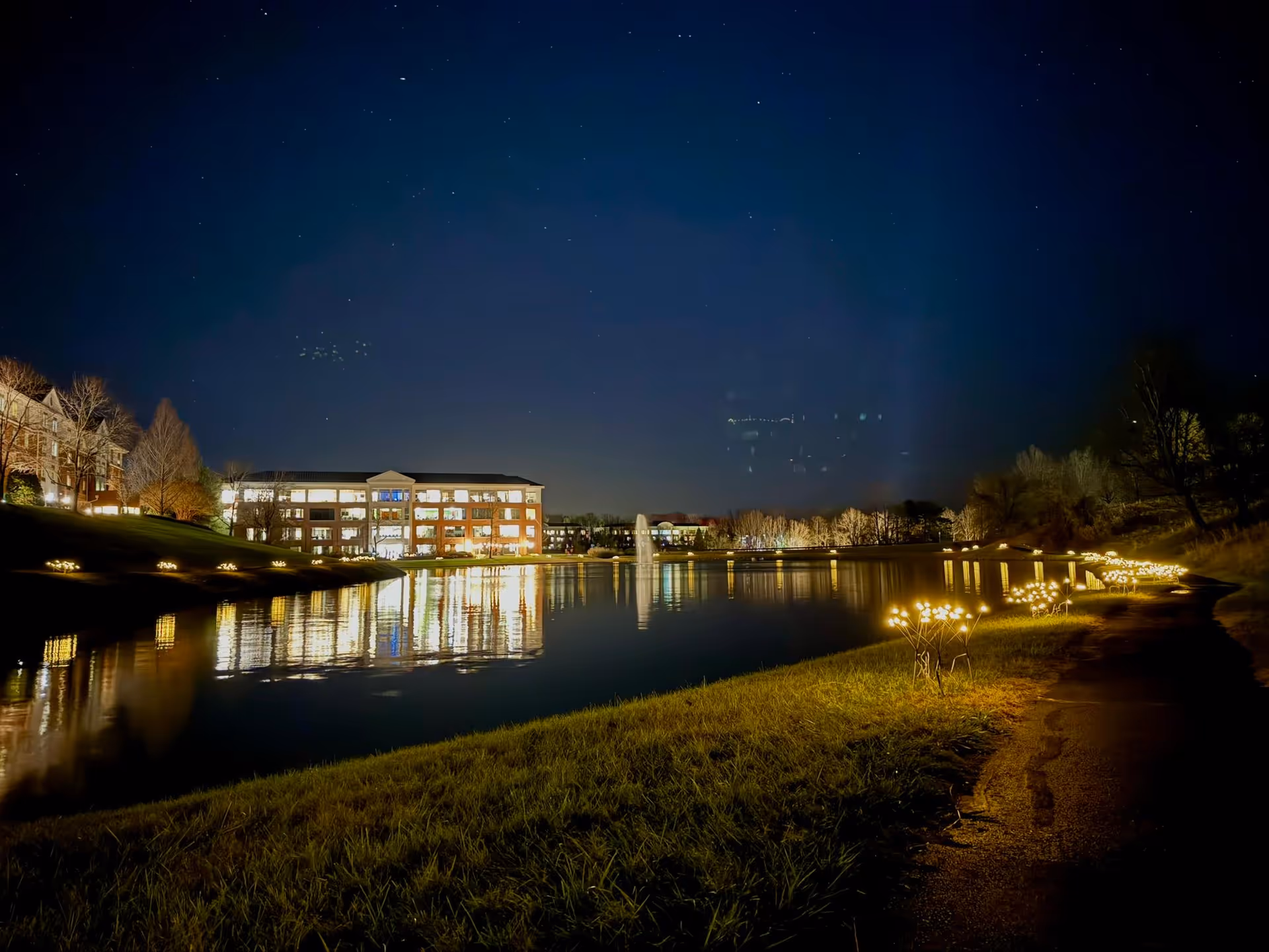 Night view of a lit senior living campus beside a reflective lake.