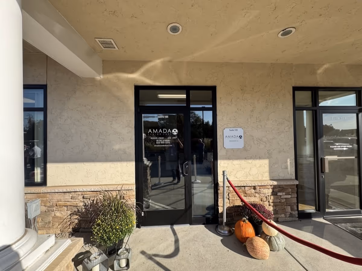 Exterior entrance of Amada Senior Care building with glass doors, pumpkins, and decorative plants