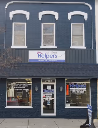 Two-story dark blue brick building with Senior Helpers sign and large storefront windows.
