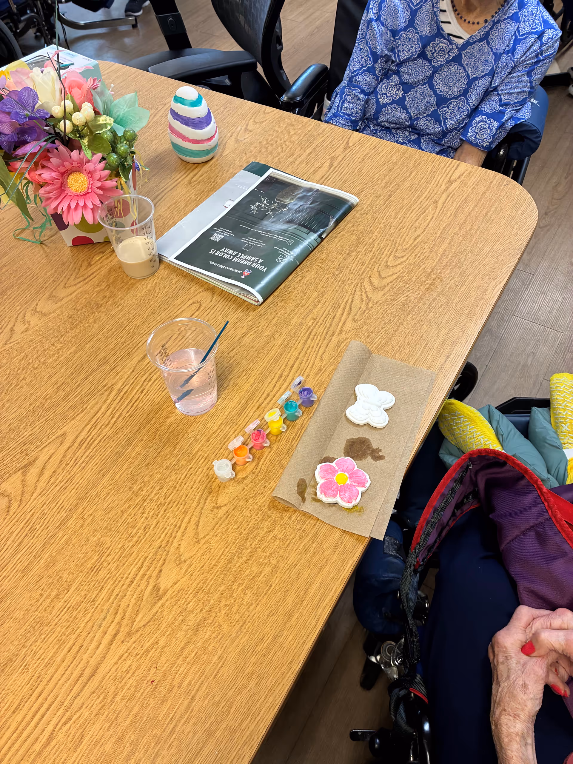 Table with crafts and a resident in a wheelchair in an indoor activity area.