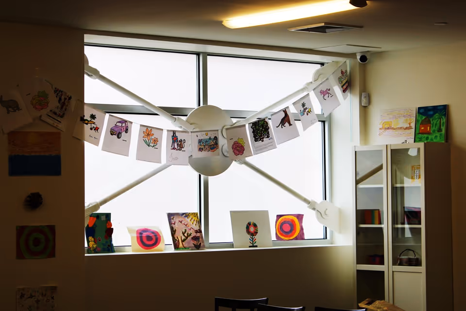 Interior activity room with hanging children's artwork along a windowed wall and central fixture.