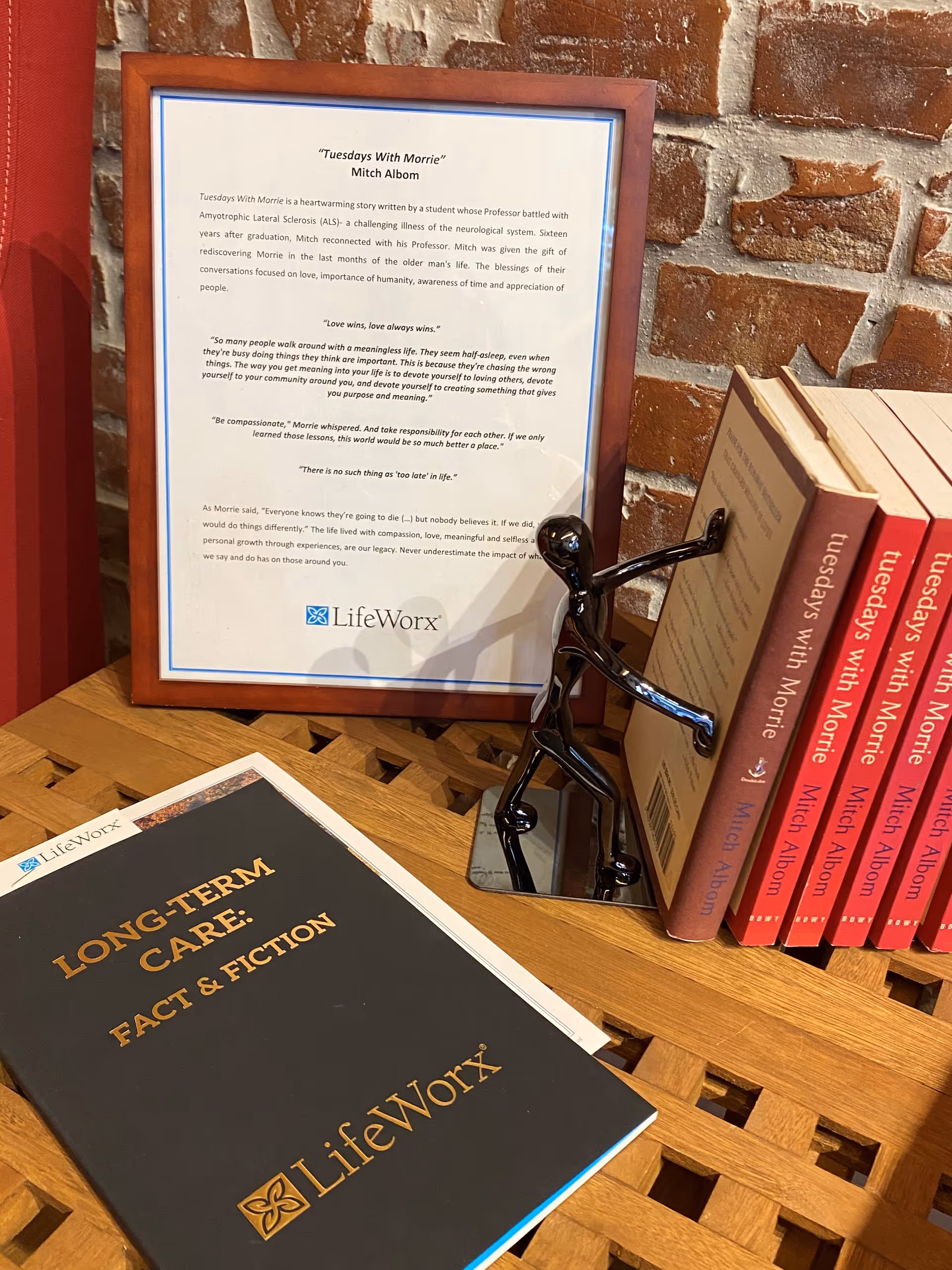 Framed LifeWorx document, LifeWorx-branded booklet, and red-spined books on a wooden lattice desk.