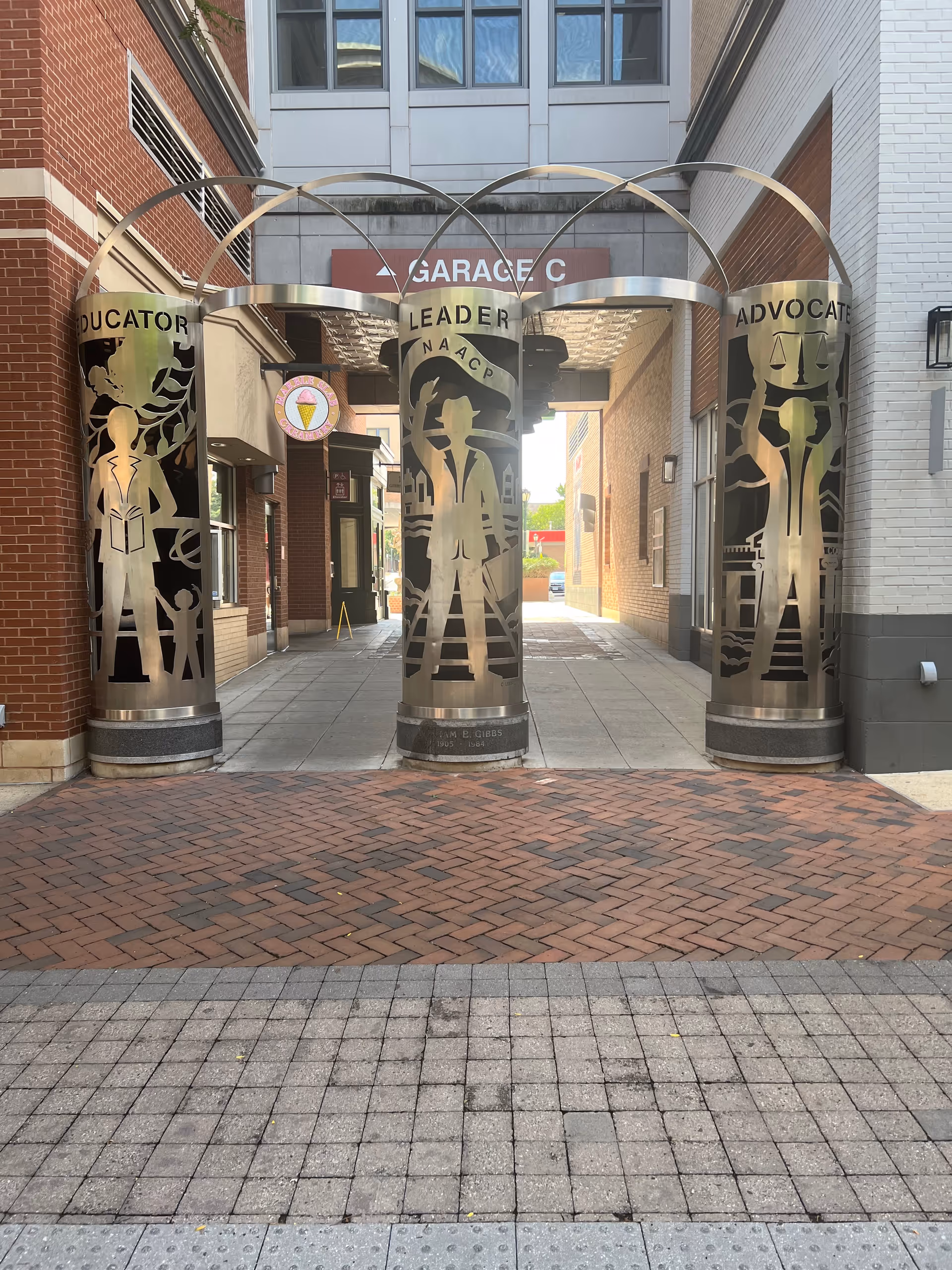 Exterior passageway near a building entrance with three large metal sculptures labeled Educator, Leader, Advocate.