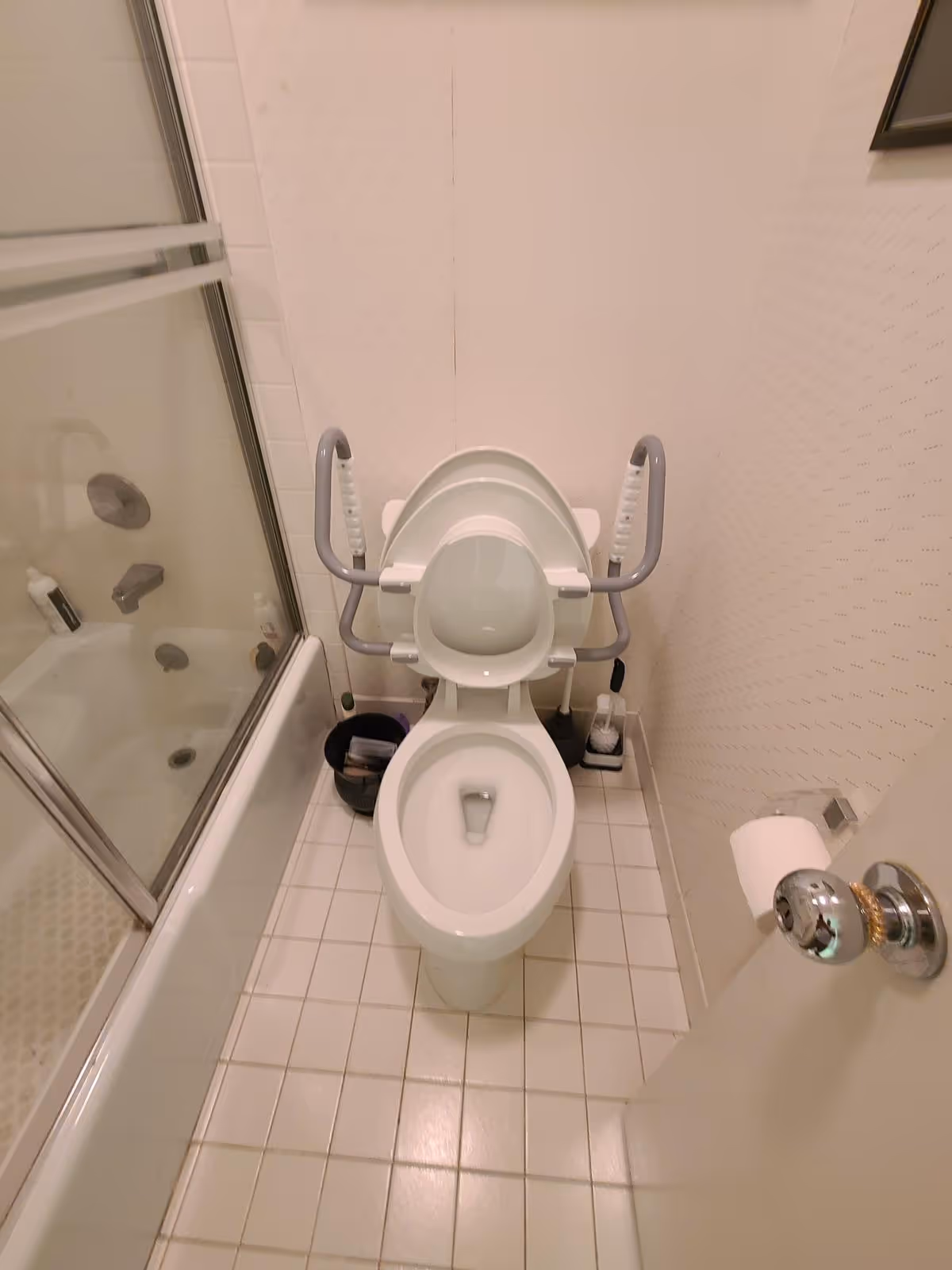 Accessible bathroom with toilet and grab bars beside a glass shower enclosure.