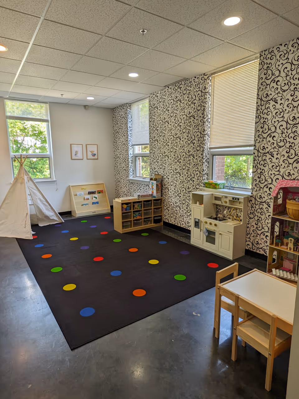 Interior playroom with a black carpet, colorful spots, teepee, and toy kitchen.
