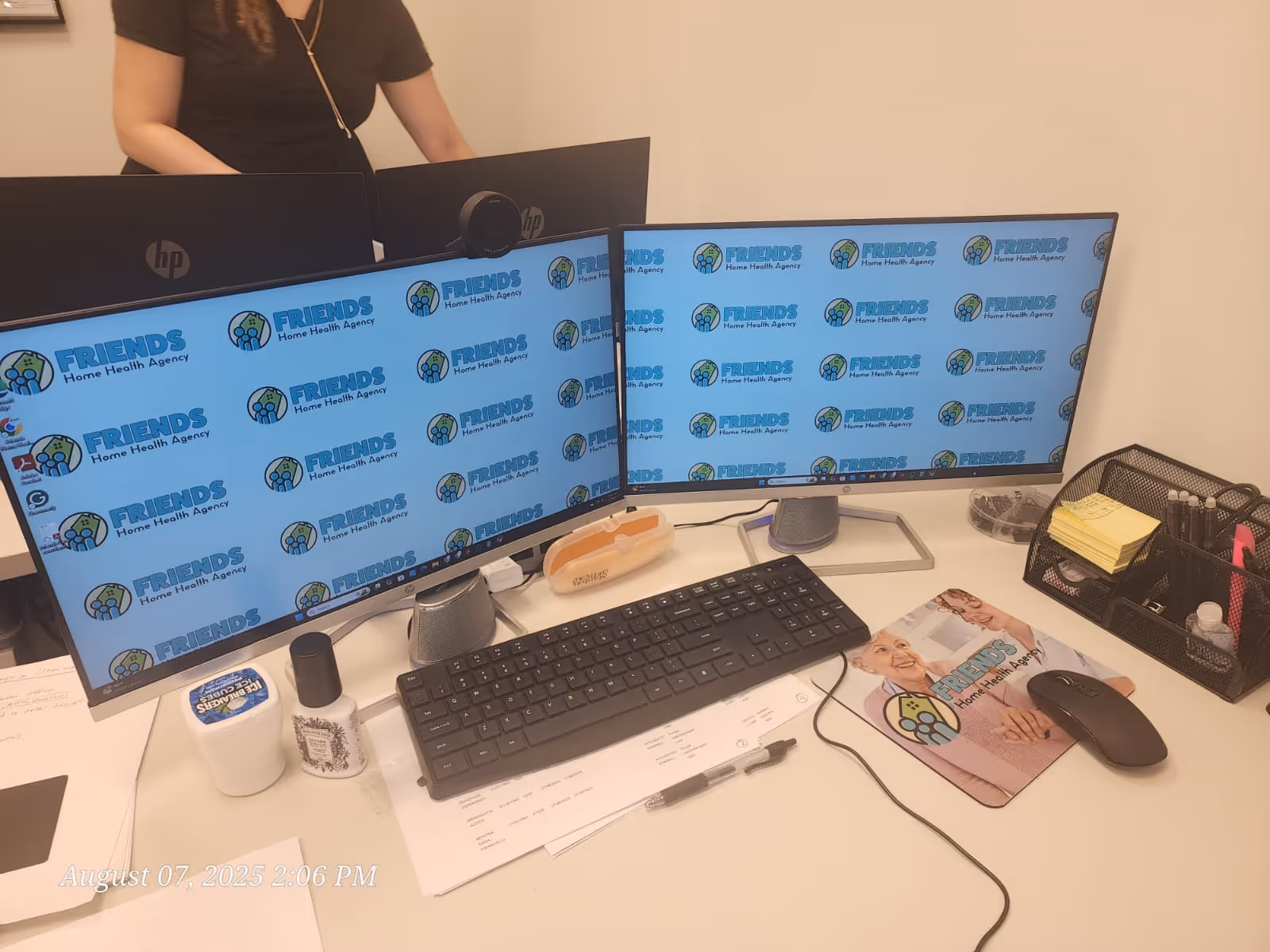 Two monitors display FRIENDS Home Health Agency branding at a desk with office supplies.