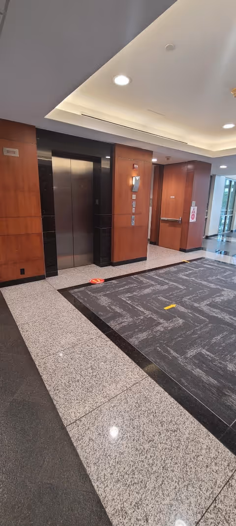 Interior hallway with elevators, wooden panels, and polished tiled floors in a modern facility.