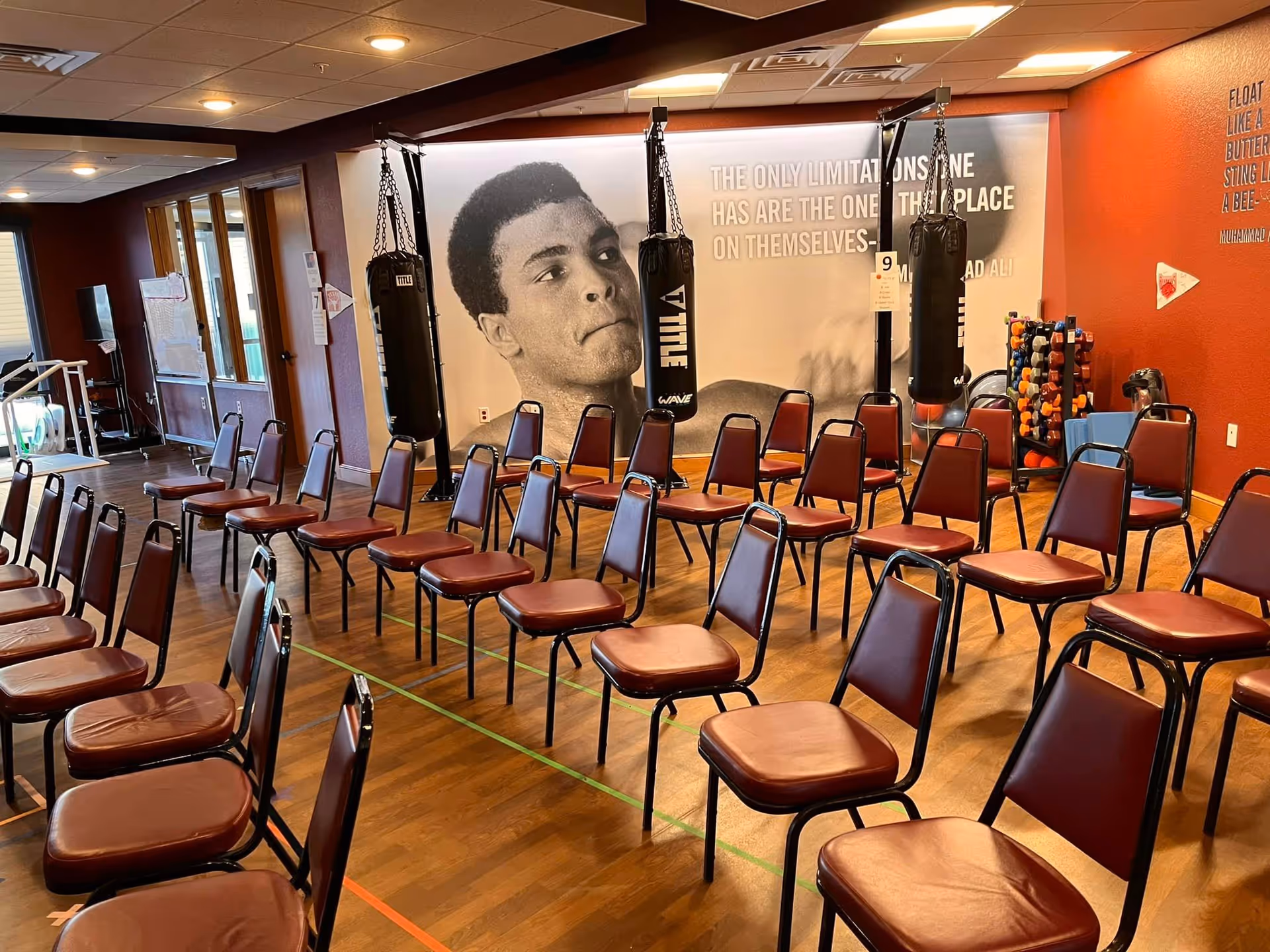 An interior multipurpose room with rows of brown chairs, punching bags, and a large mural.