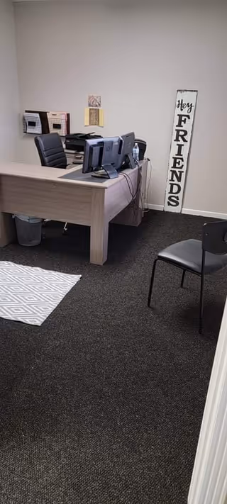 A small office area with a wooden desk, computer, and Hey Friends sign.