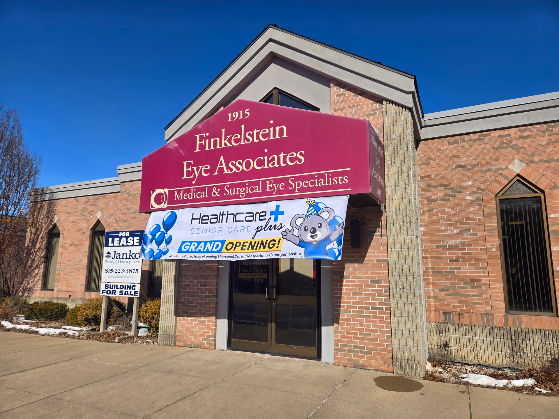 Brick storefront with a large maroon Finkelstein Eye Associates sign and a grand opening banner.