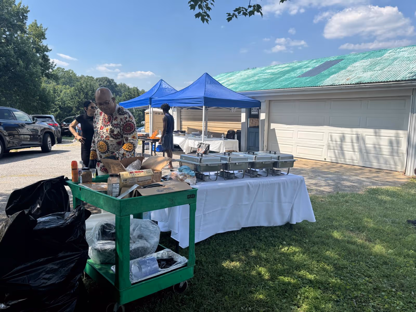 Outdoor catering setup with chafing dishes under a blue canopy beside a building.