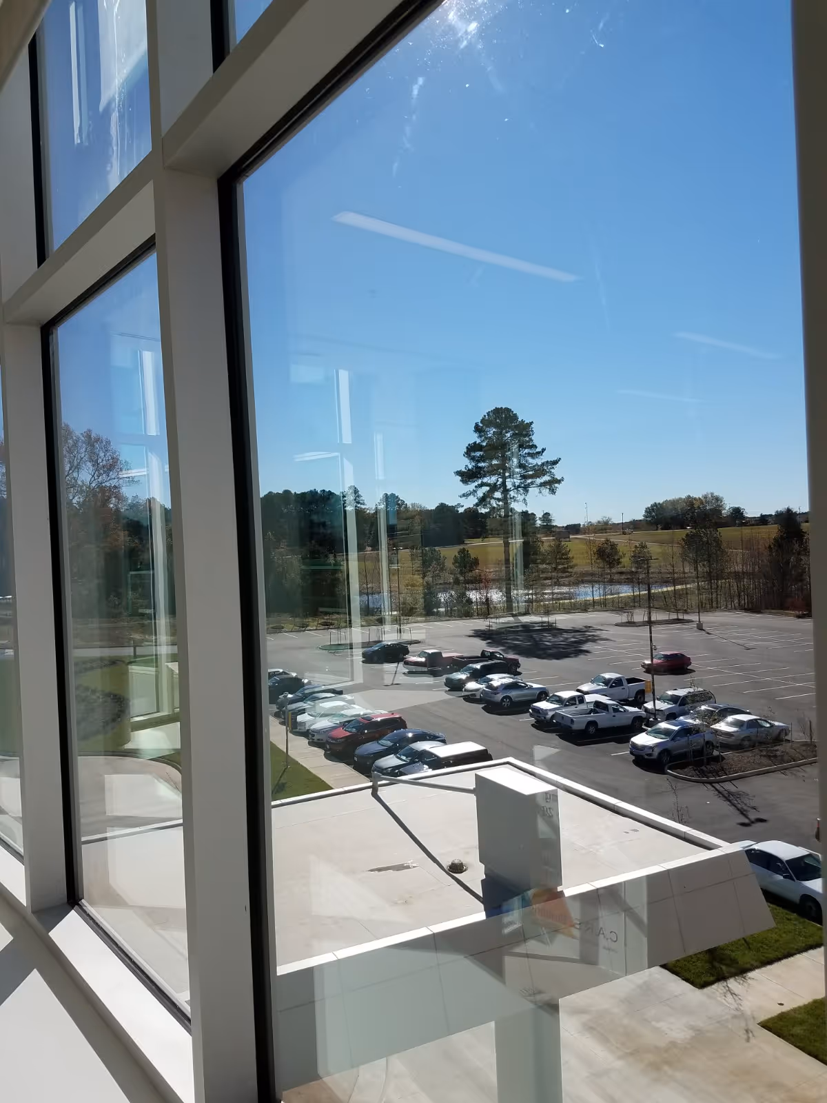 Interior view with tall windows overlooking a parking lot and trees outside.