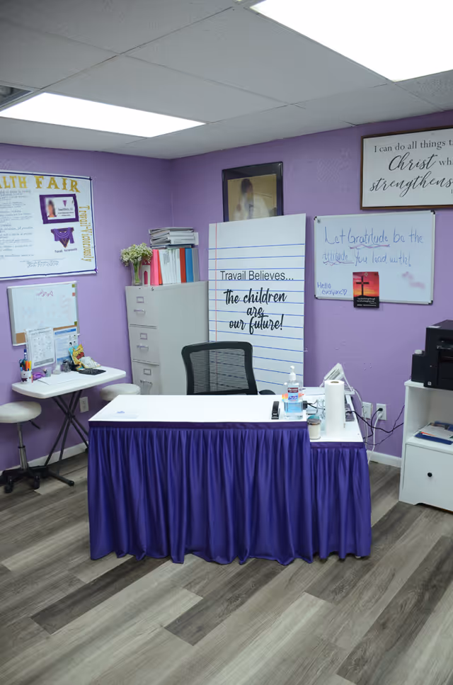 Purple-walled indoor office with a desk, chair, and purple-skirted table in a facility.