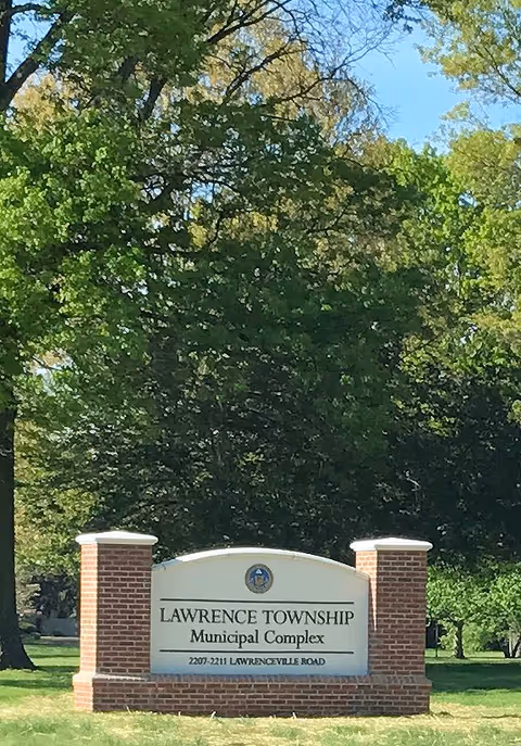 Outdoor sign for Lawrence Township Municipal Complex framed by brick pillars and trees.