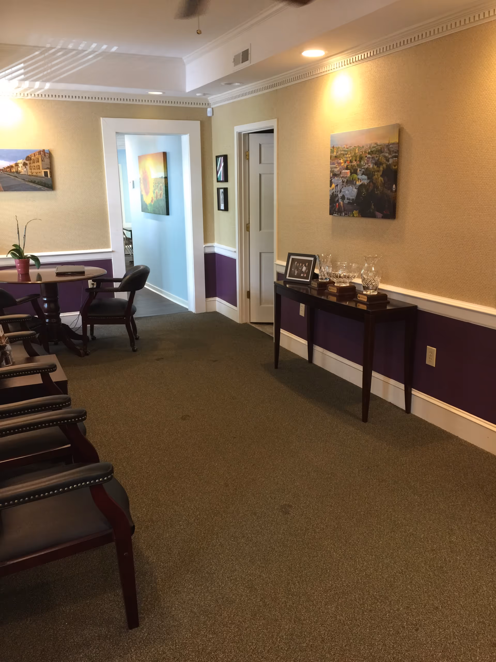 An interior hallway in a senior living facility with purple wainscoting, chairs, and a console table.