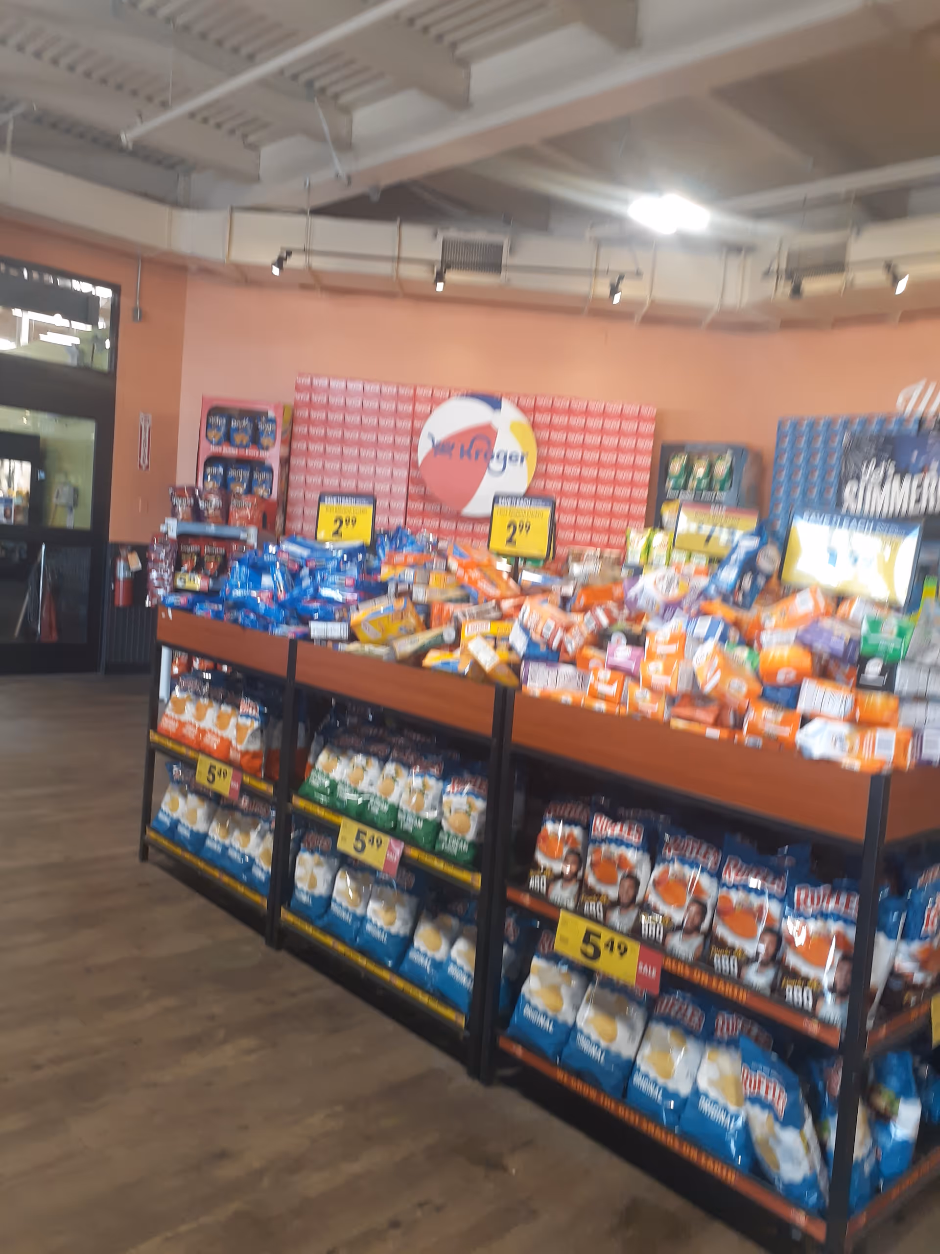 Inside a Kroger Pharmacy, shelves filled with snacks and drinks near a pink wall with logo.