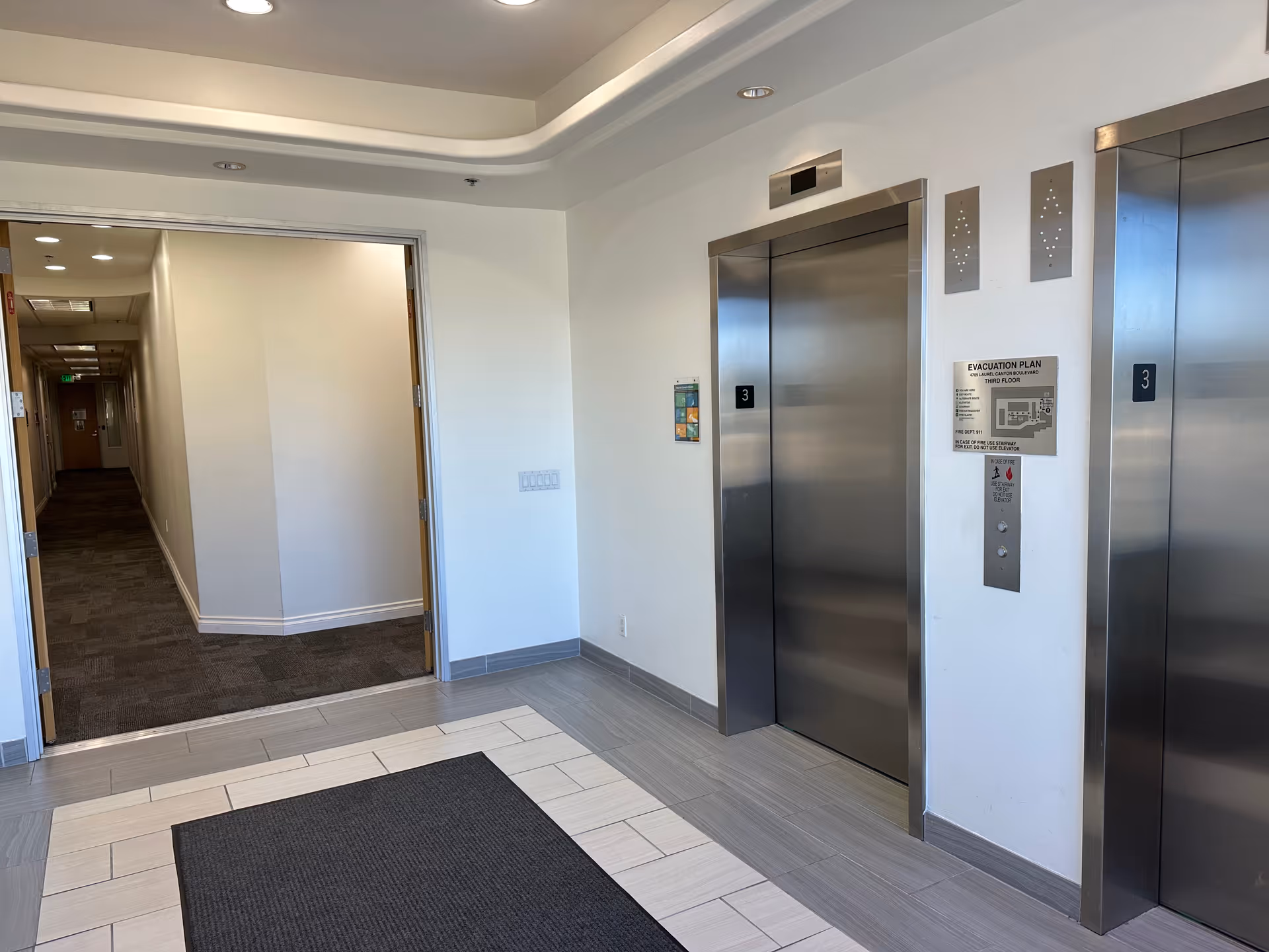 Interior hallway near two elevators with tiled floor and carpeted corridor.