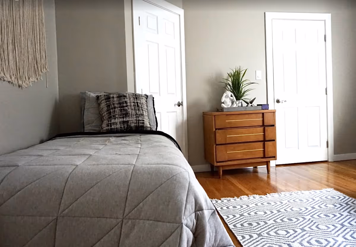 Cozy bedroom in a senior facility with a bed, dresser, plant, doors, and rug.