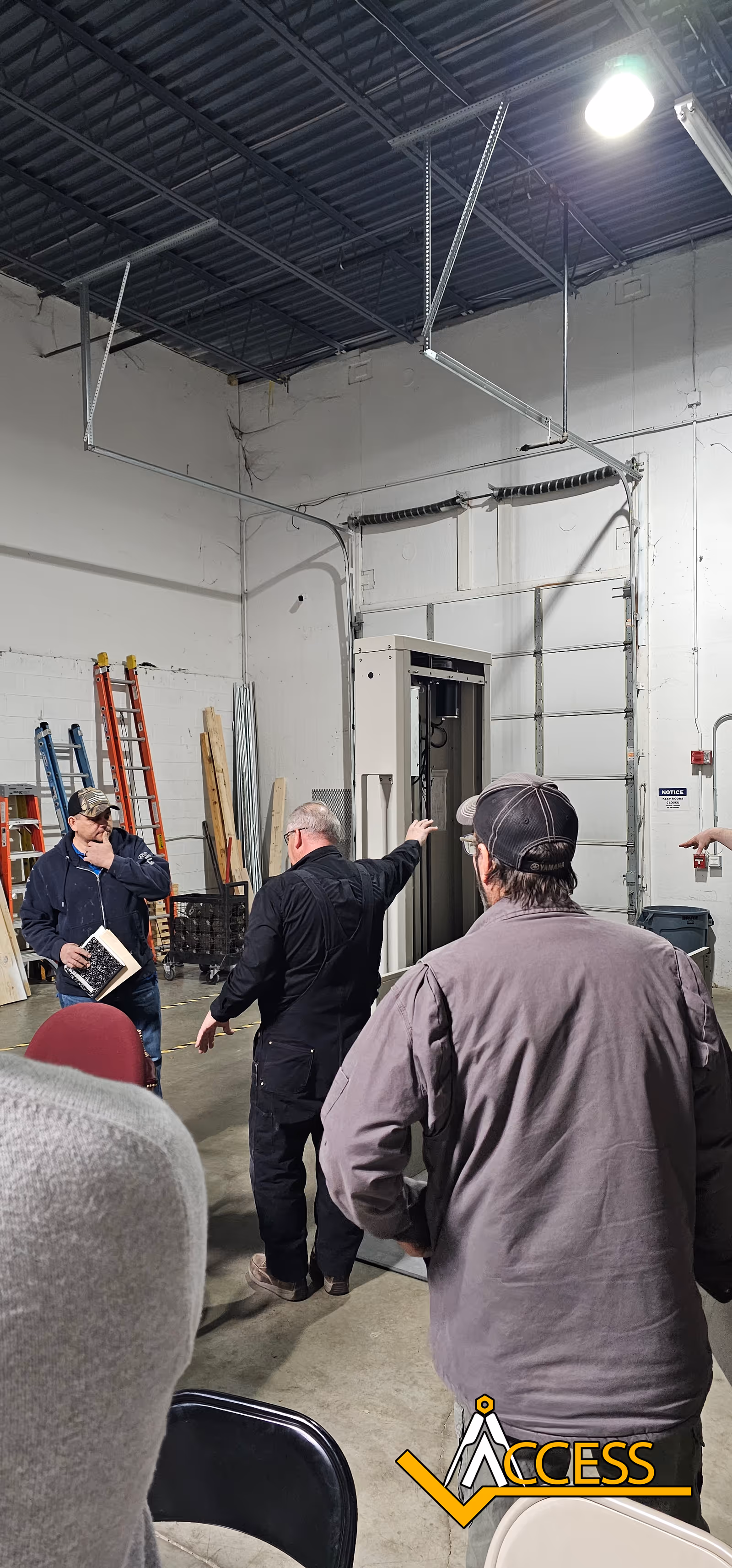 Industrial interior with workers, ladders, and a control cabinet.