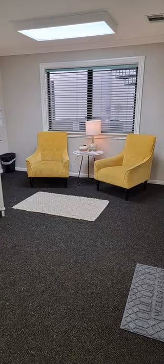 Two yellow armchairs flank a small table with a lamp in a bright waiting area.