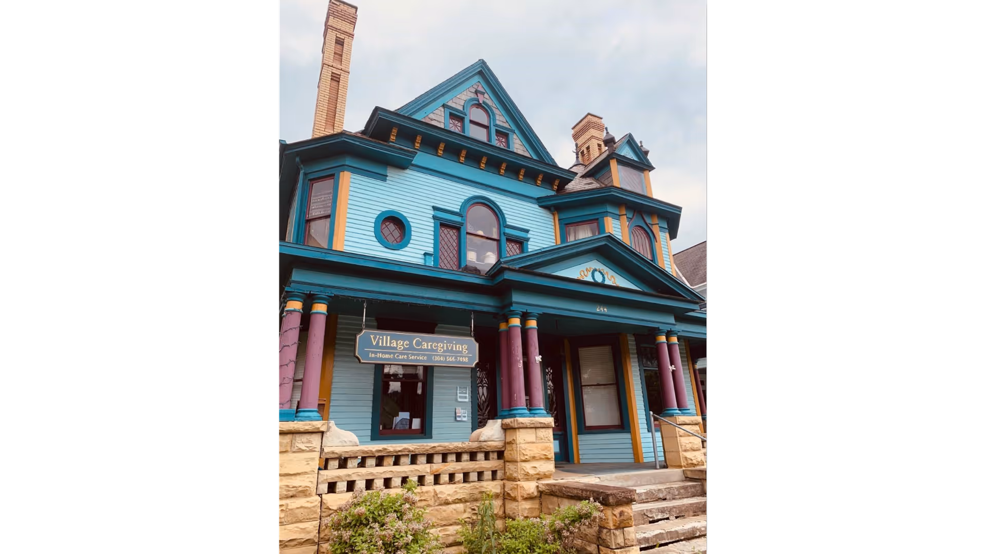 Colorful Victorian-style care facility building with a sign reading Village Caregiving at the entrance.