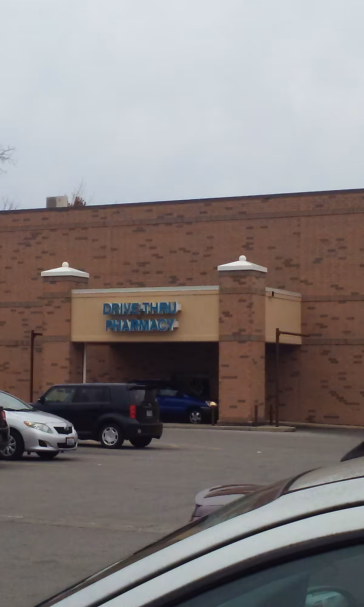 Brick Kroger Pharmacy drive-thru entrance with parked cars in the lot.