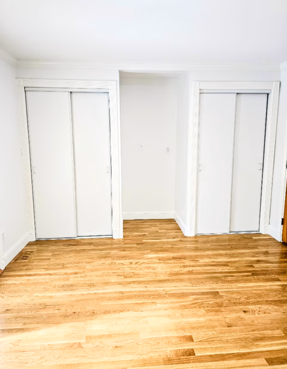 Bright empty hallway featuring two closet doors and a central alcove; wood floor.