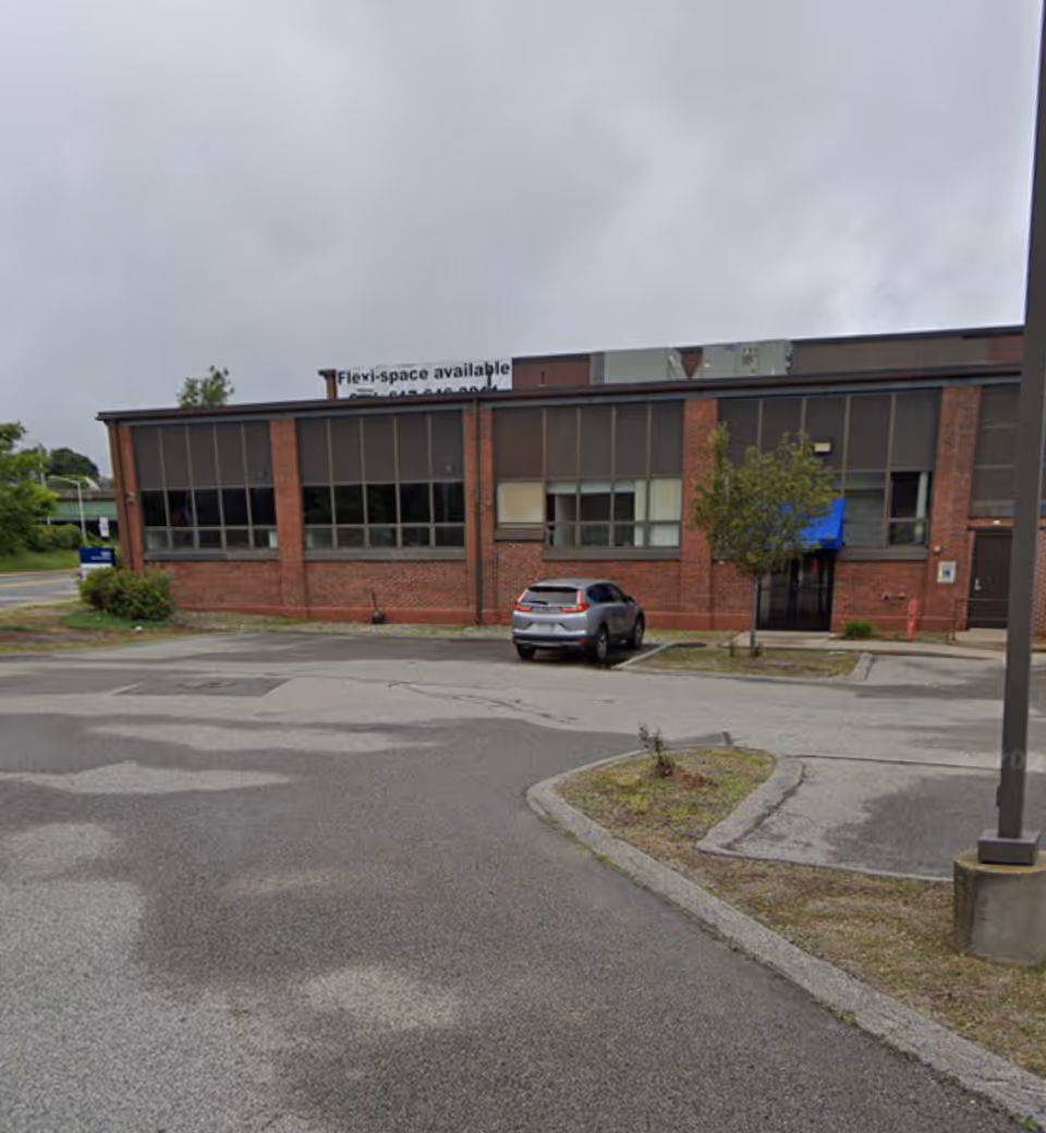 Brick building with large windows, blue awning, and a car parked in front.