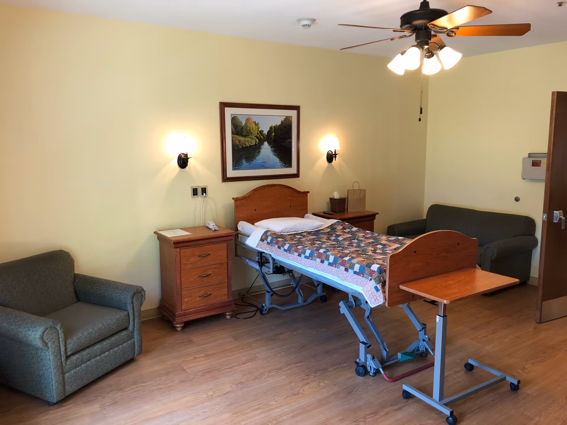 Hospital bed in a cozy bedroom with two nightstands, a couch, and a ceiling fan.