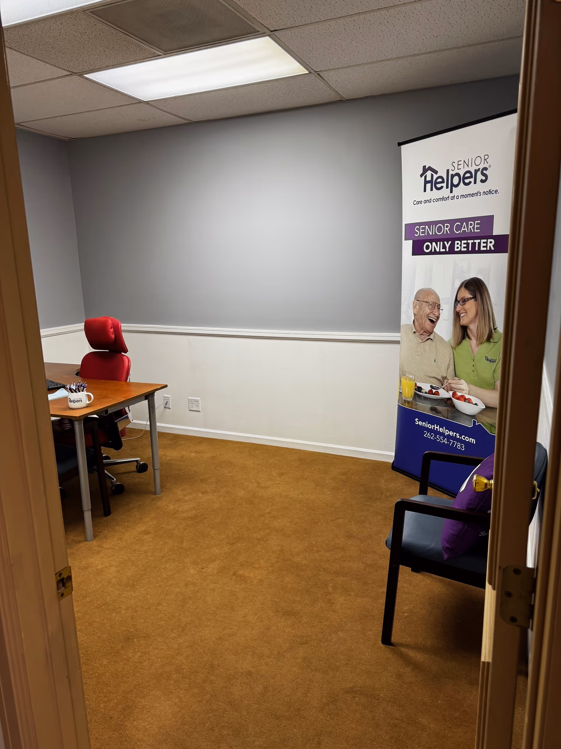 Small office-like room with a desk, red chair, and Senior Helpers banner.