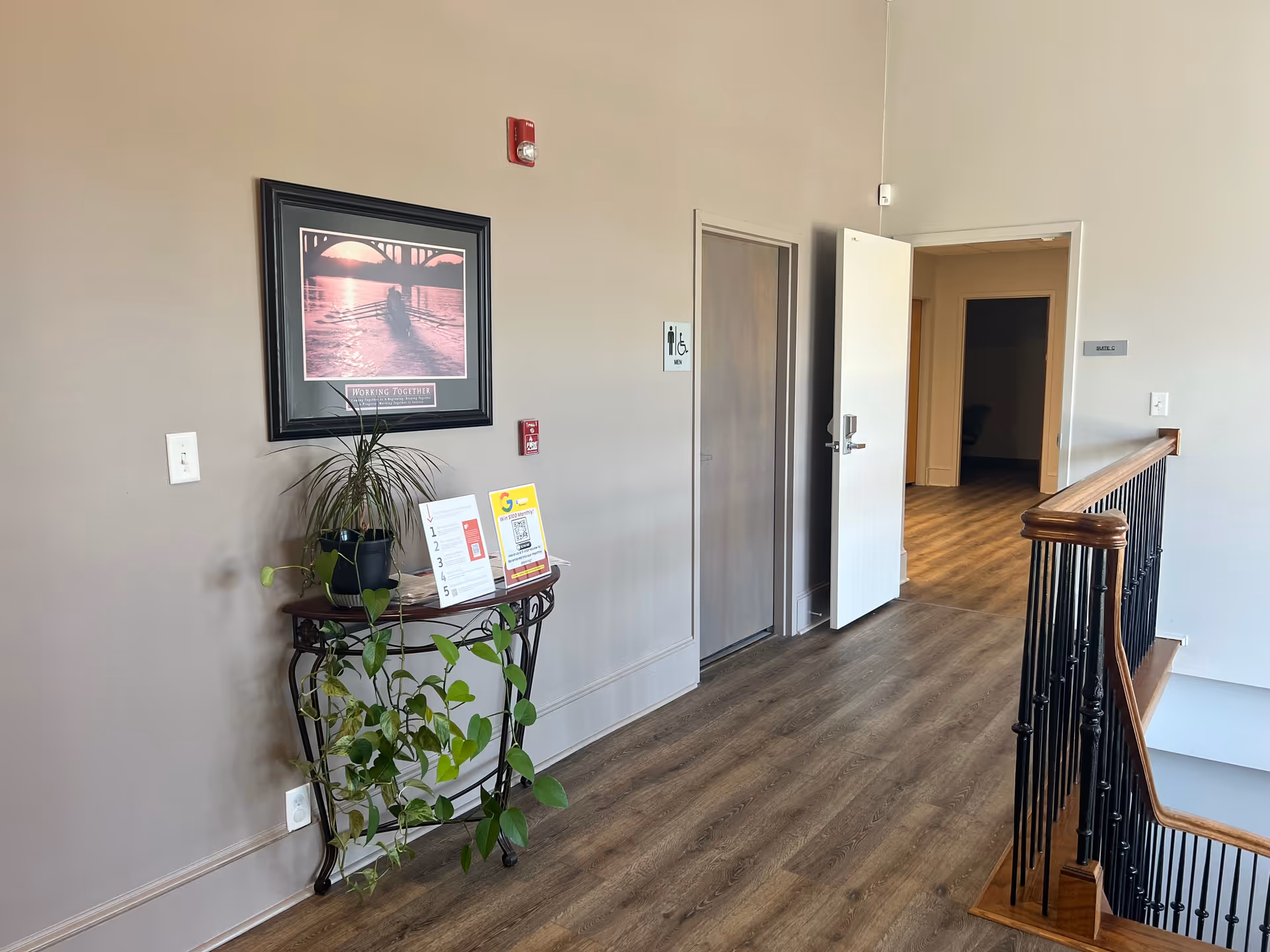 Indoor hallway in a senior living facility with plants, framed art, and an open door.