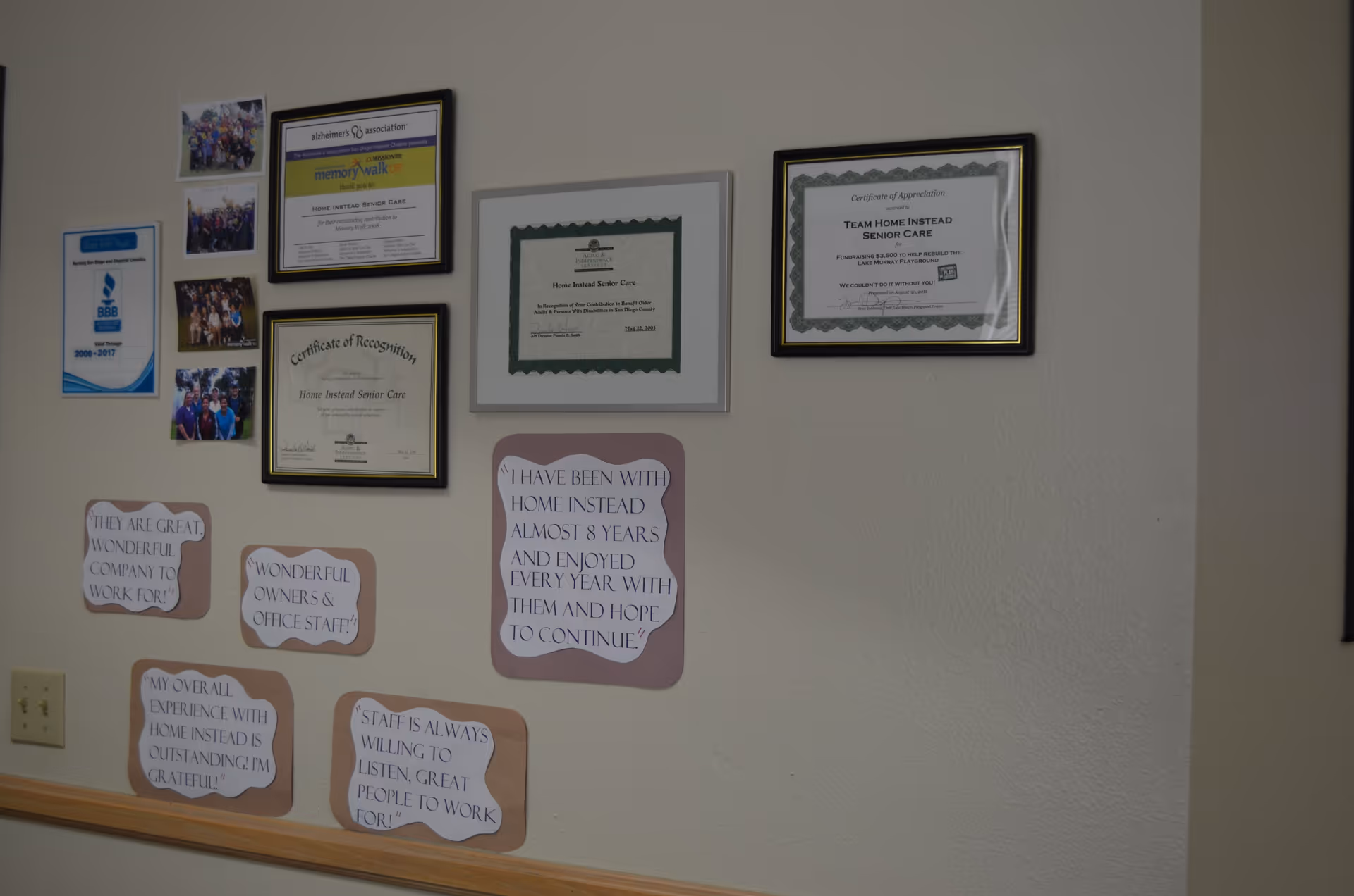 Wall interior with framed certificates, photos, and motivational quotes displayed in a senior care facility.