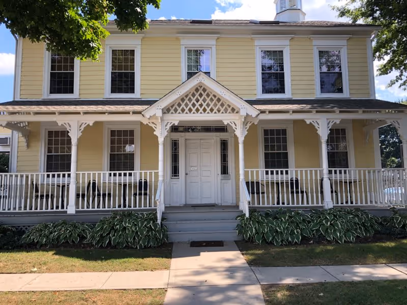 Yellow two-story senior living facility with a white wraparound porch and decorative trim.