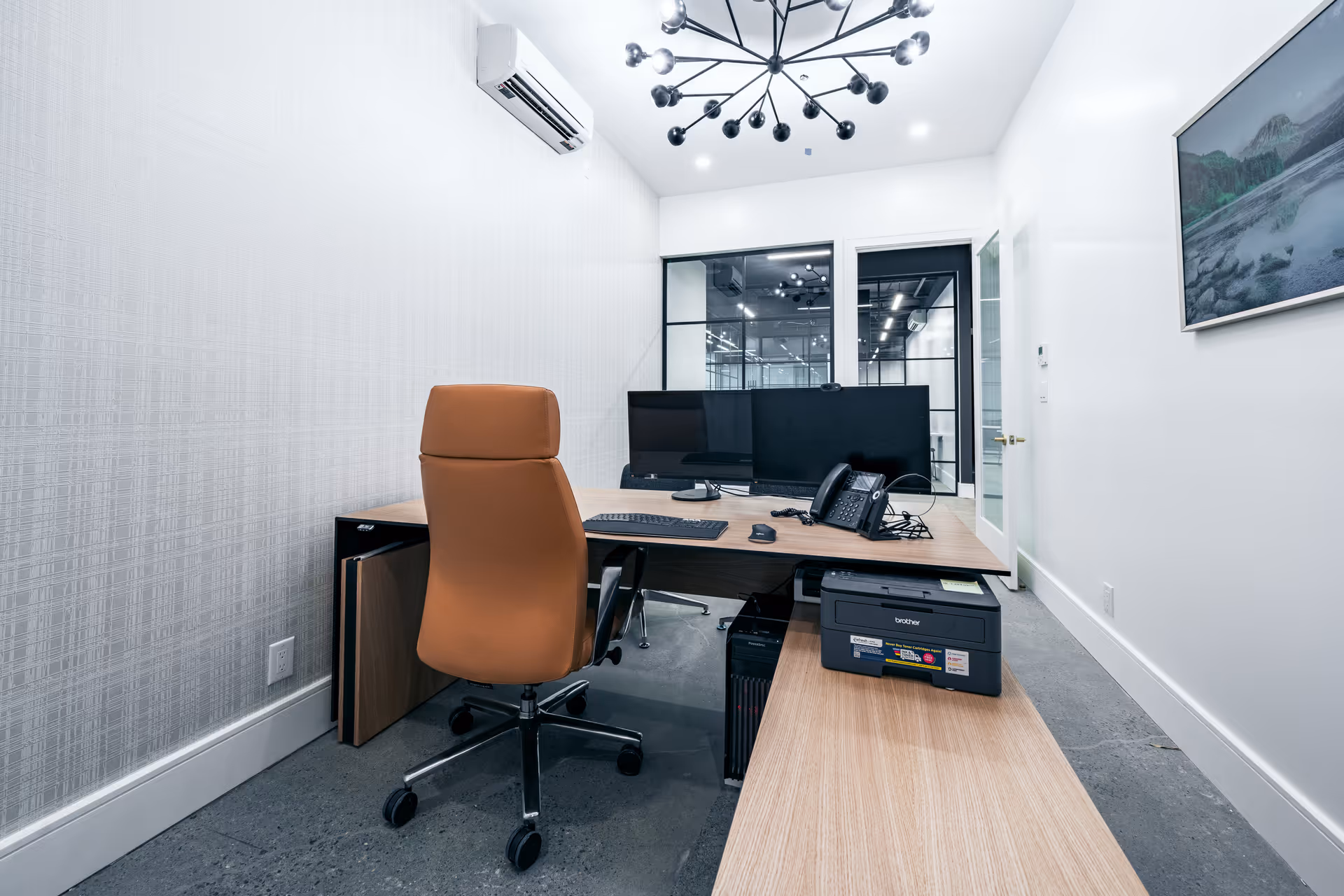 Modern office with desk, chair, dual monitors, phone, and printer in a bright, clean room.