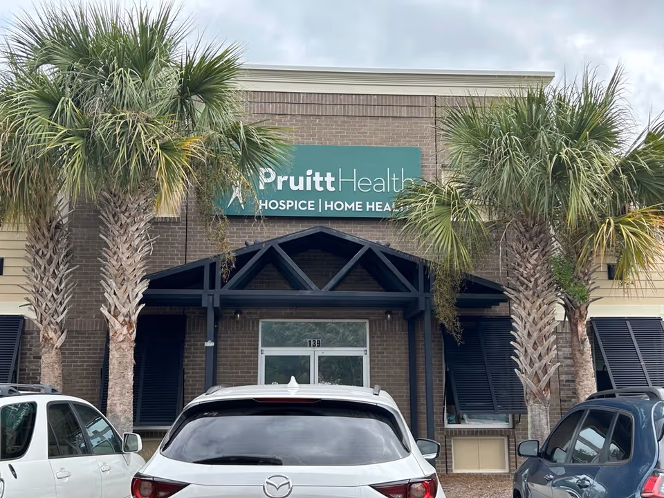 Exterior view of PruittHealth at Home Charleston building with palm trees and parked cars.