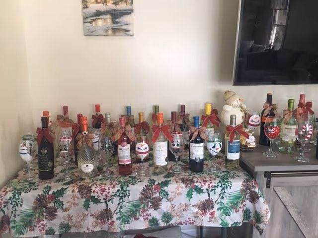 Table covered with a festive tablecloth displays numerous wine bottles wrapped with ribbons.