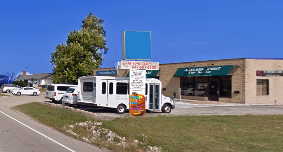 Exterior view of a strip mall with a white shuttle bus parked in front.
