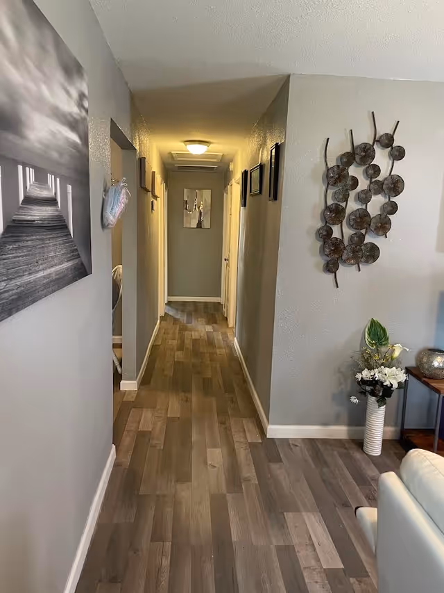 Interior hallway of a senior living facility with wall art, laminate flooring, and seating.