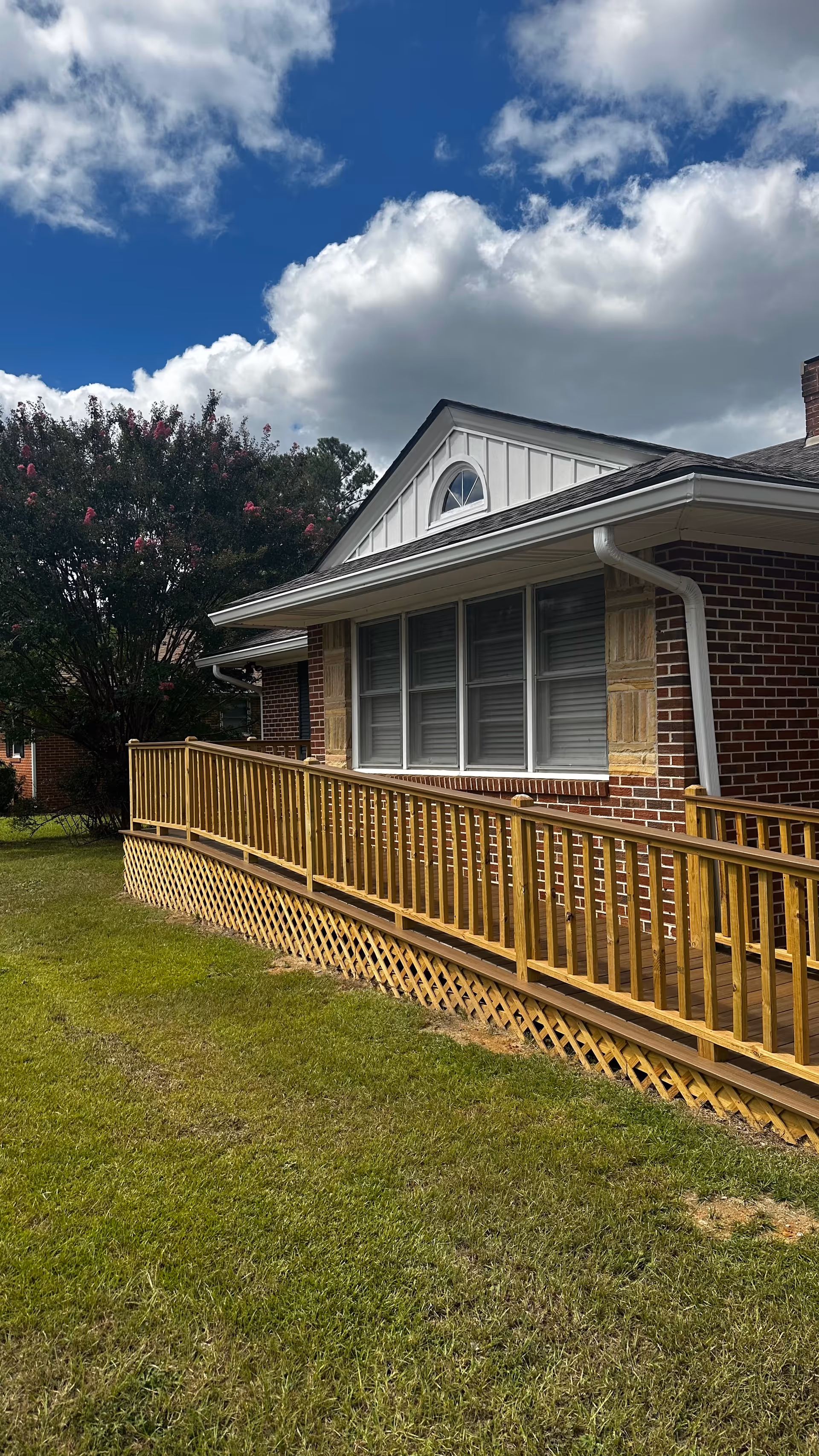 Brick senior care facility exterior with a wooden ramp, grassy yard, and cloudy sky.