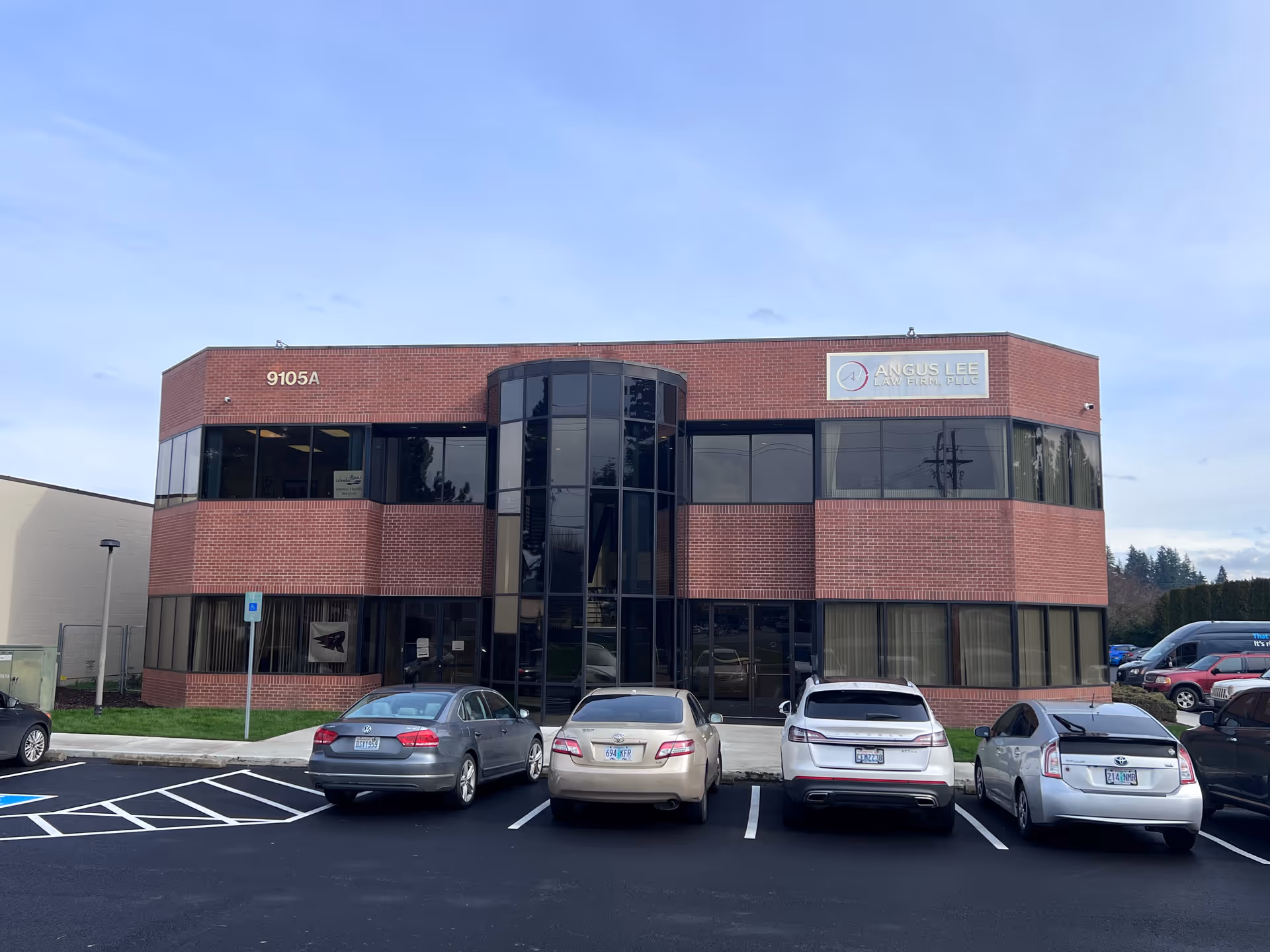 Two-story brick office building with curved glass entry and parked cars in front.