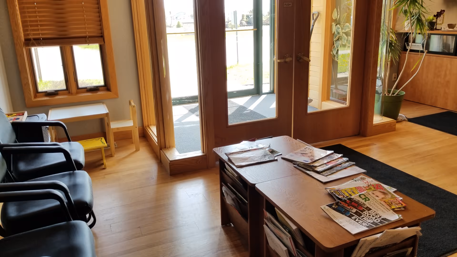 Waiting area with chairs and magazines near glass doors in a hallway.