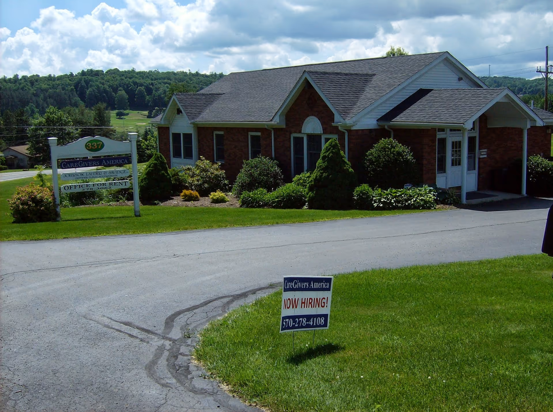 Brick, single-story CareGivers America facility with manicured lawn and a hiring sign.