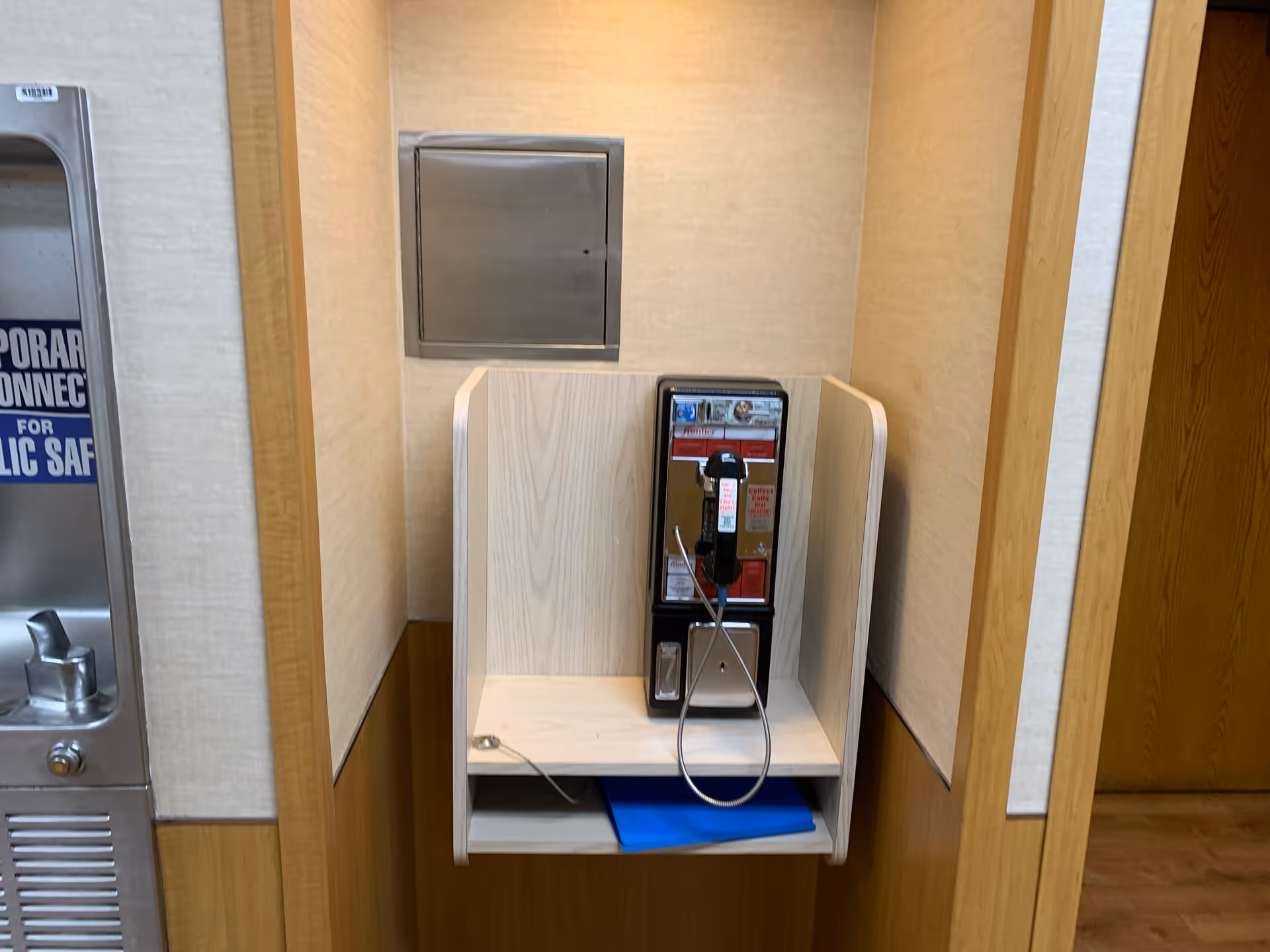 Inside a hospital hallway alcove, a wall-mounted phone on a small shelf.