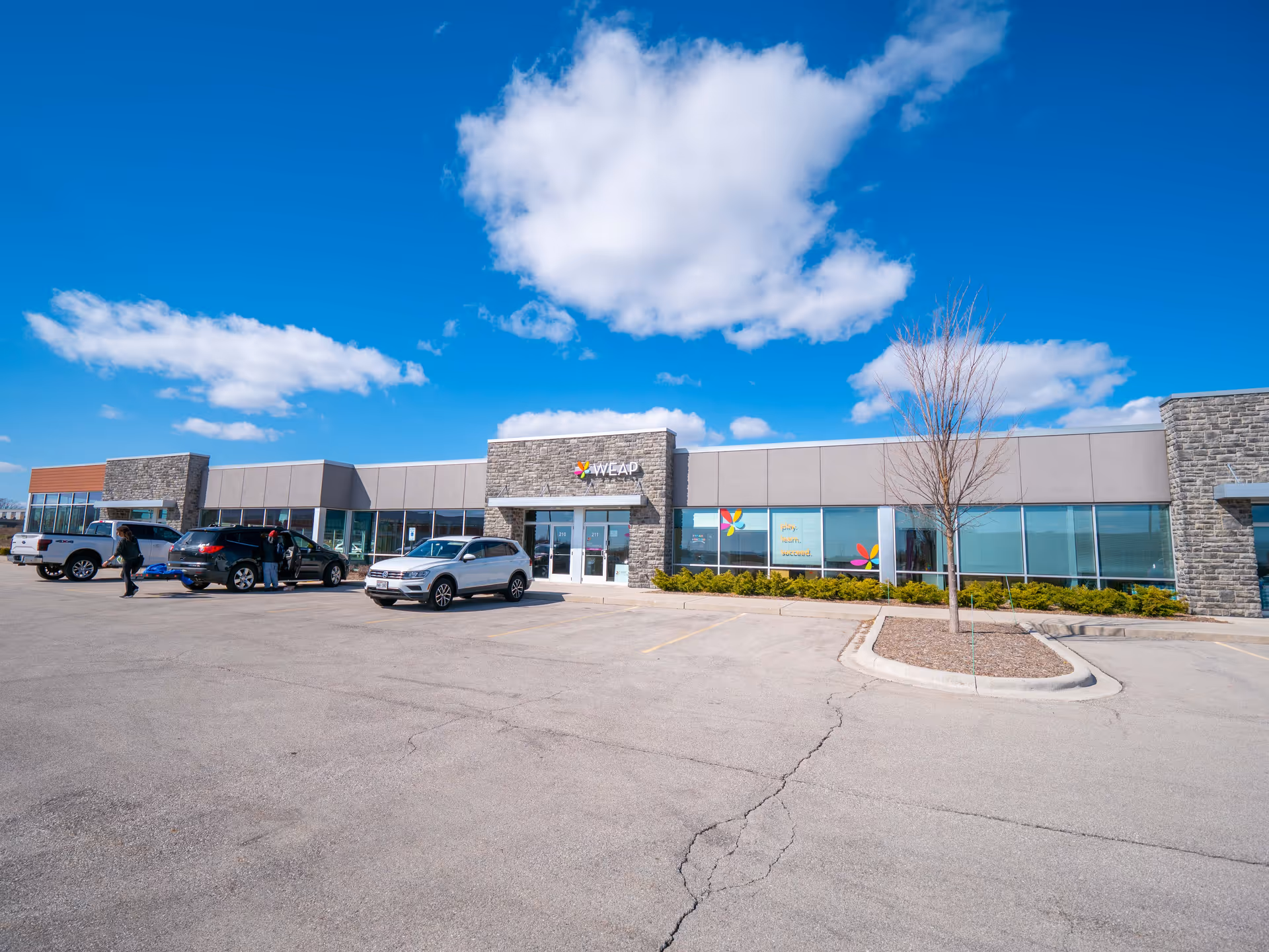 Modern single-story facility with WEAP sign and parked cars in lot.
