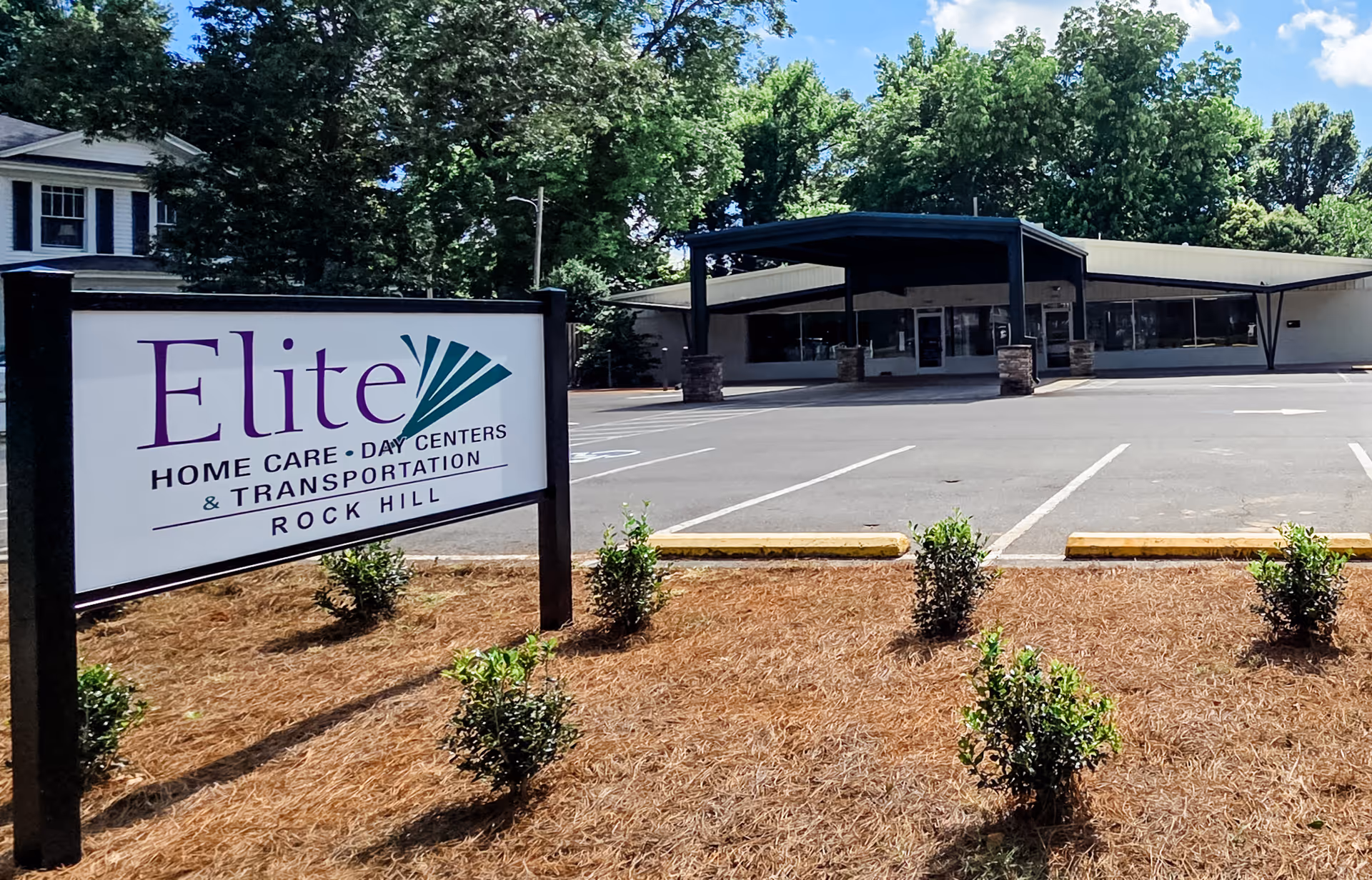 A sign for Elite Home Care and Day Centers outside a building with a parking lot.
