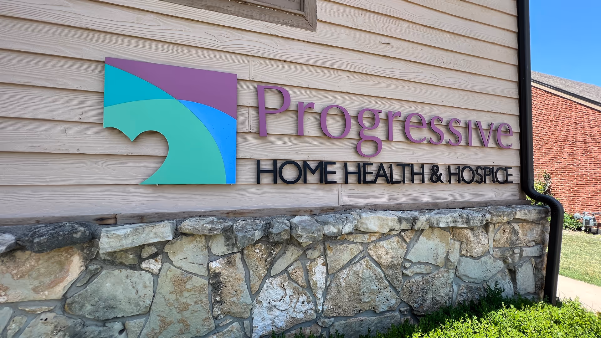 Exterior wall of Progressive Home Health & Hospice with colorful sign and stone foundation.