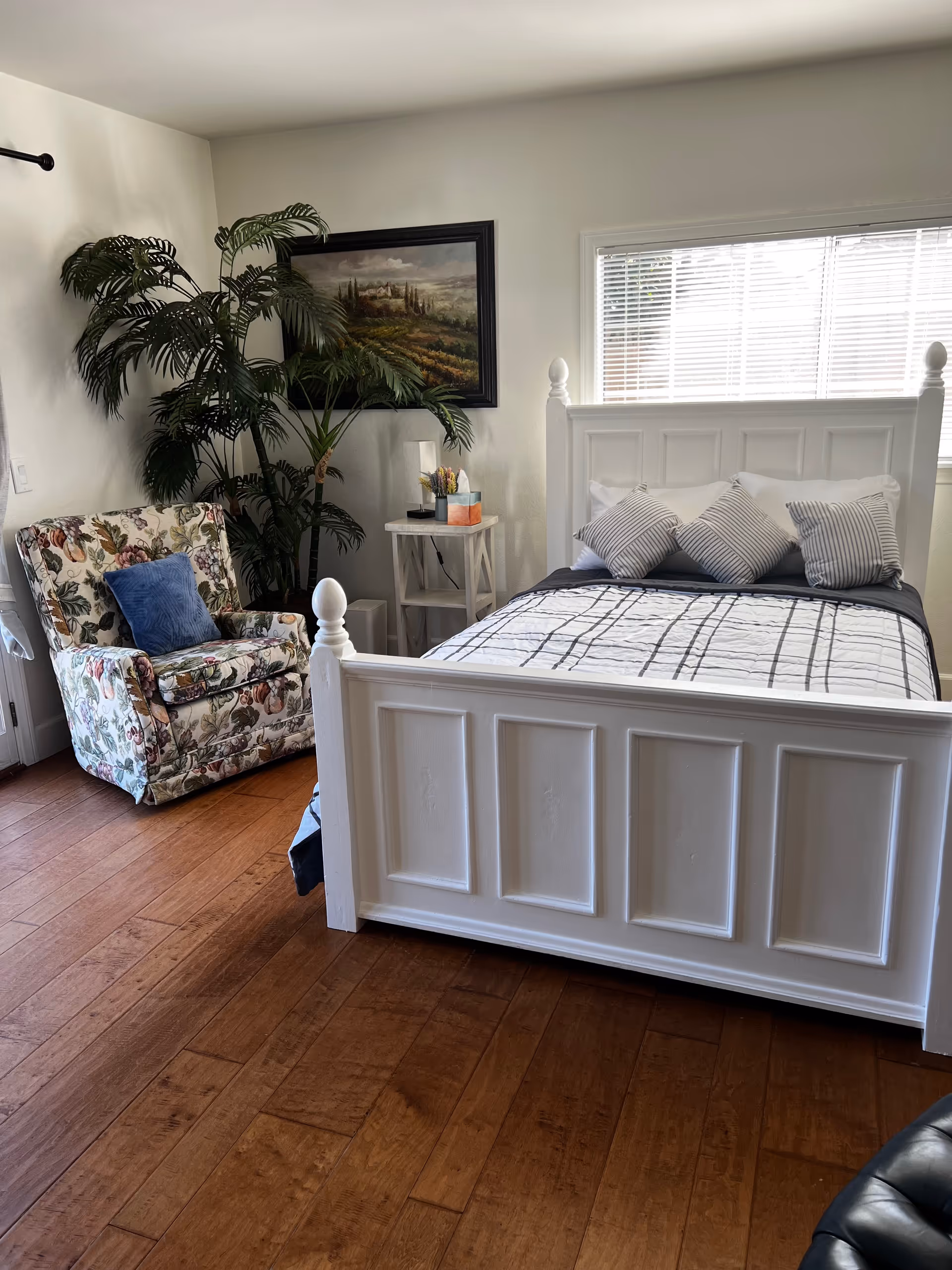 White paneled bed, striped pillows, floral armchair, and nightstand in a bright bedroom.