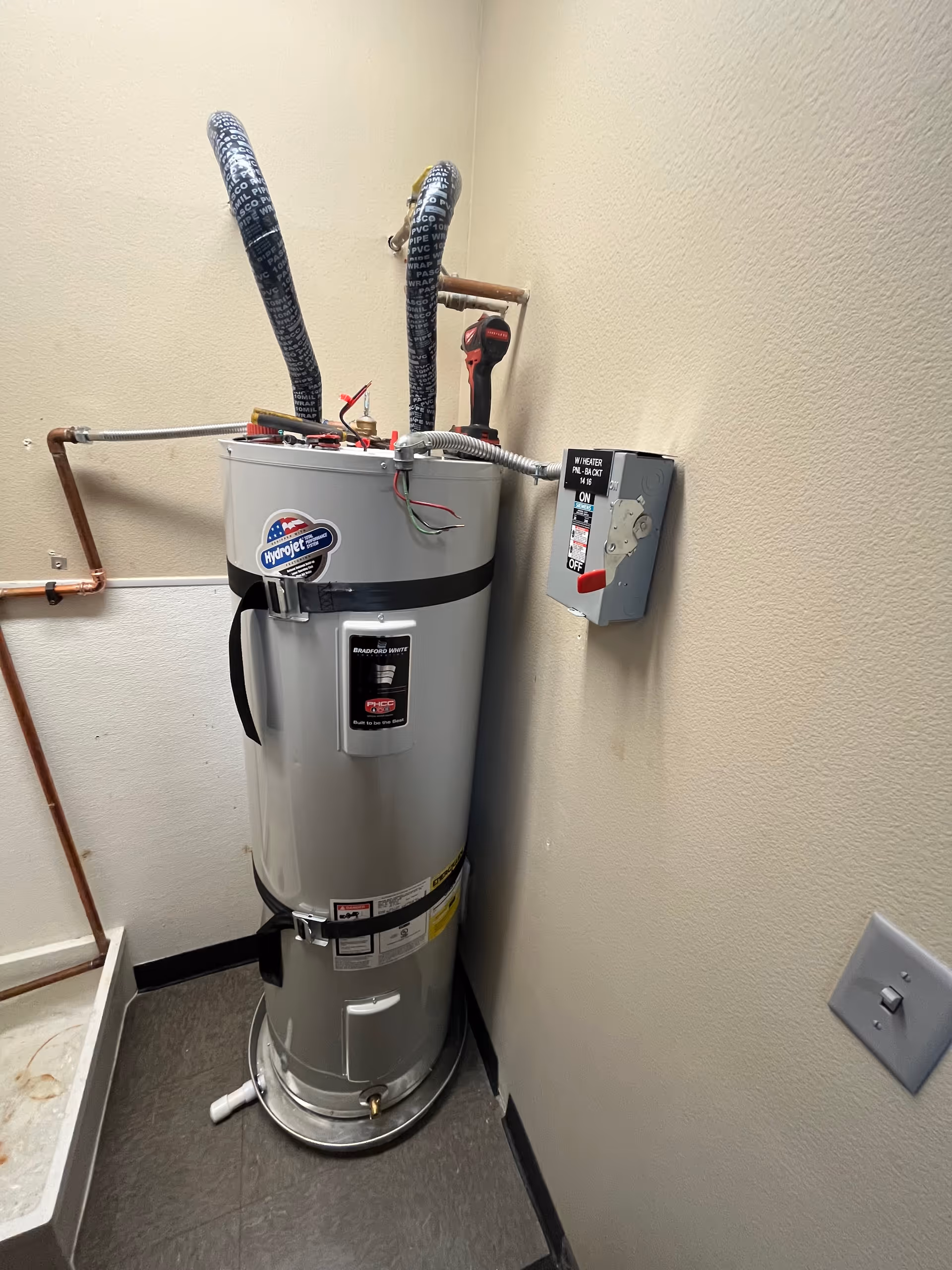 Tall water heater in a small utility closet with exposed pipes.